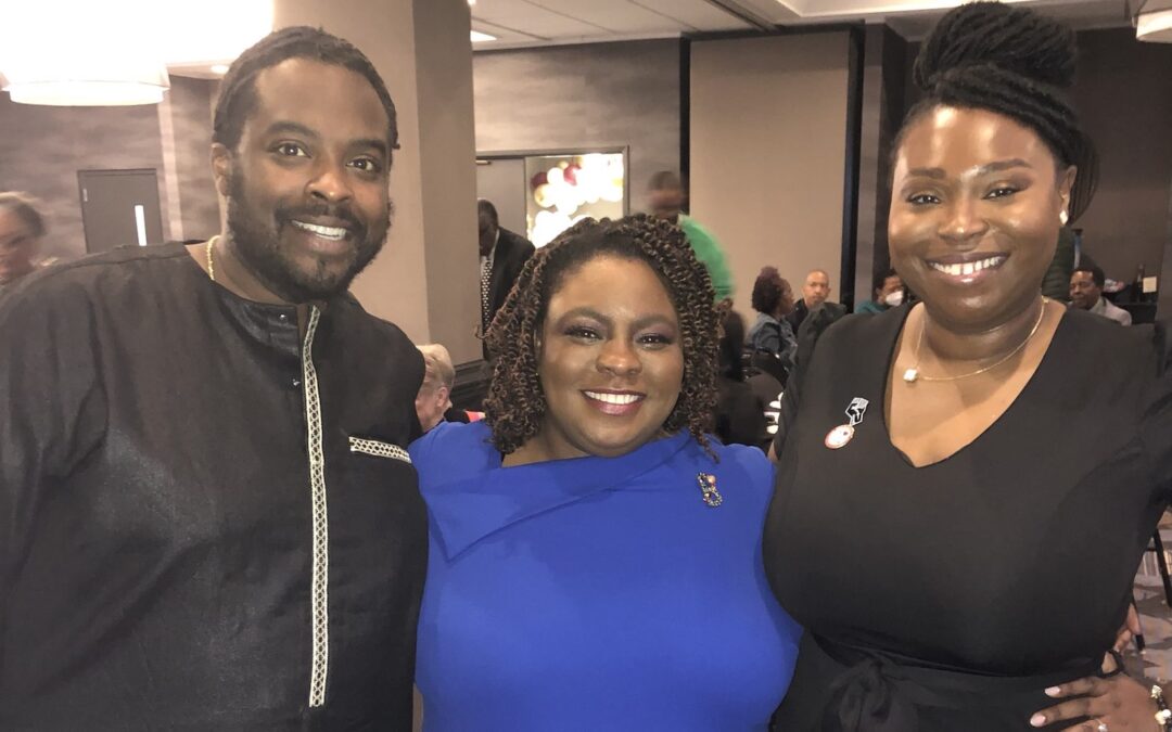 Emancipate ED Dawn Blagrove, a Black woman wearing a blue dress, stands between two Black colleagues, a man and a woman, smiling at the Color of Change Black History Now awards ceremony.